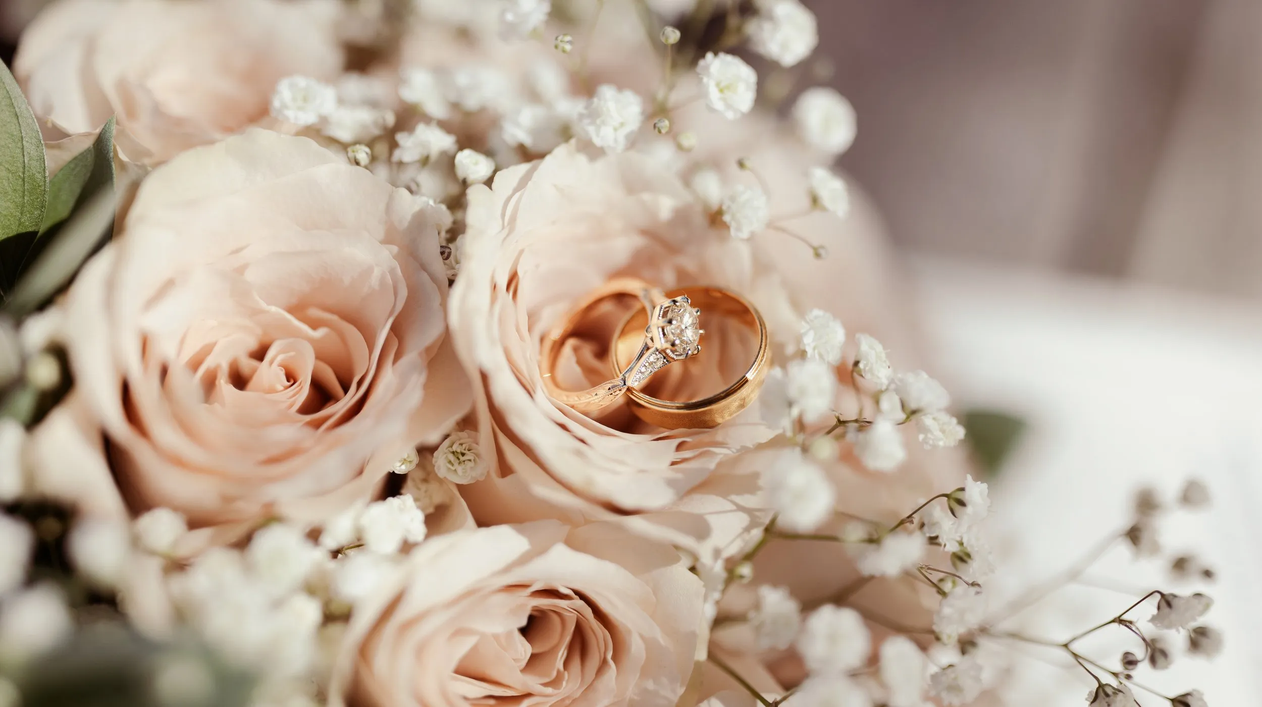 Two wedding rings resting among pale roses and gypsophila